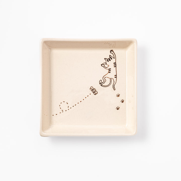 Beige square plate featuring a tabby cat chasing a butterfly with dotted trail and small paw prints.