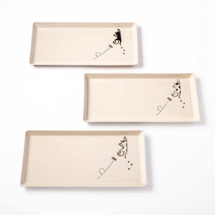 Set of beige rectangular ceramic plates featuring playful black, calico, and tabby cat illustrations with paw prints and butterflies.