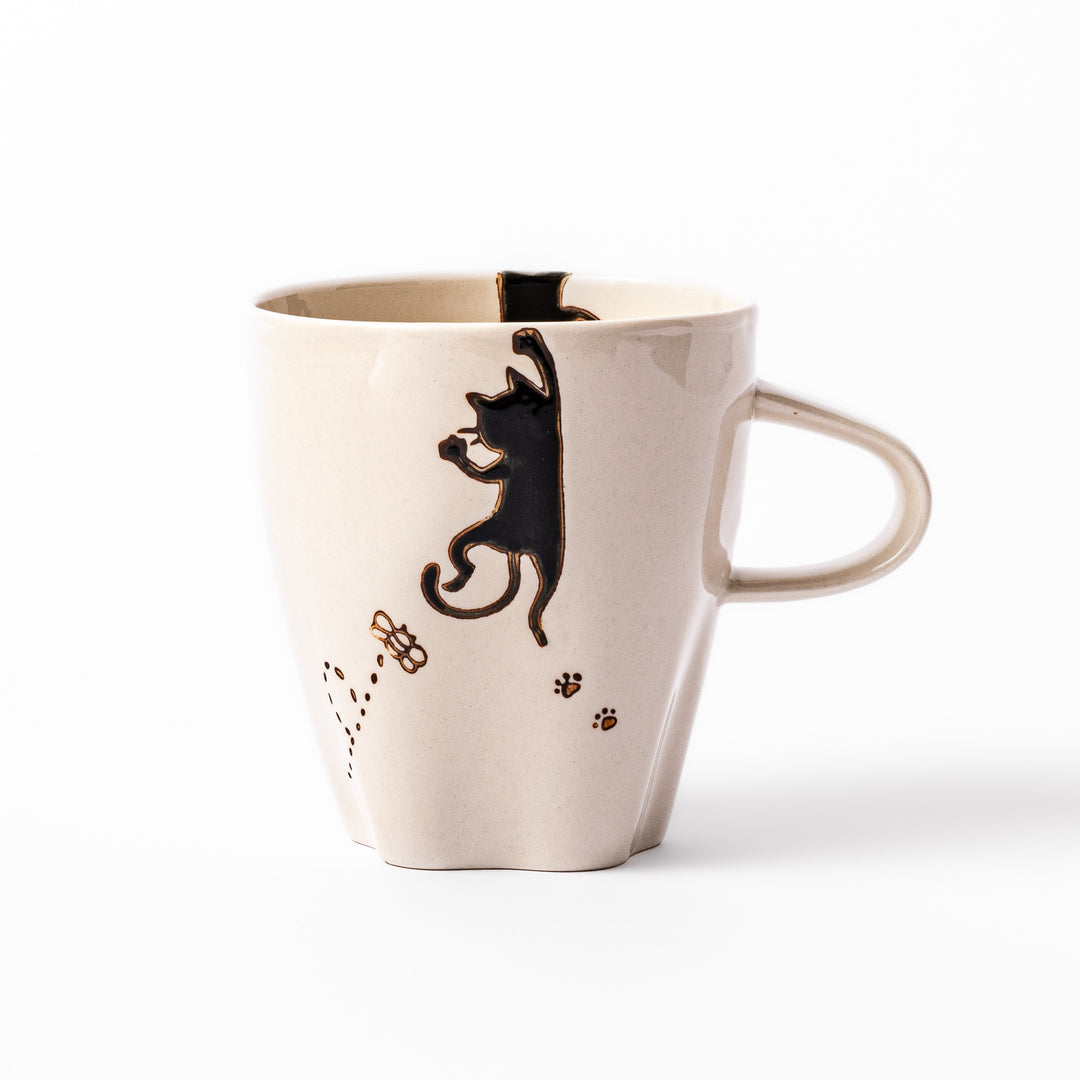 Cream-colored cup with a black cat design reaching for a butterfly, accented by playful dotted lines and paw prints.
