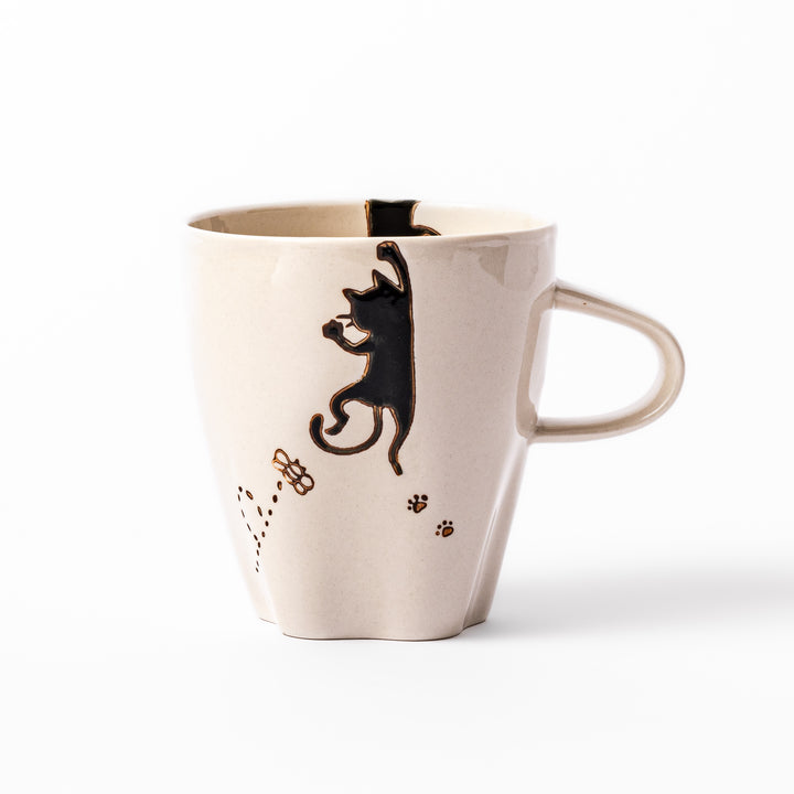 Cream-colored cup with a black cat design reaching for a butterfly, accented by playful dotted lines and paw prints.