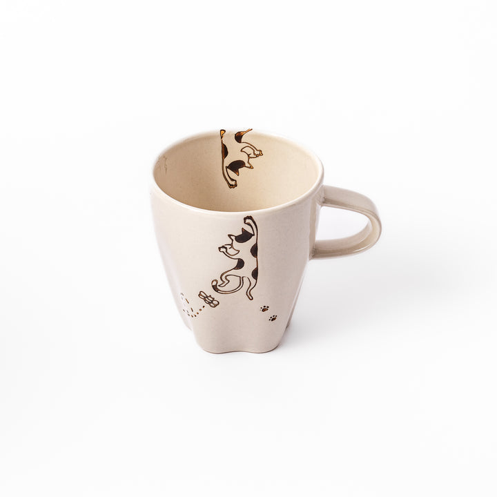 Cream-colored cup with a calico cat design reaching for a butterfly, decorated with dotted lines and paw prints.