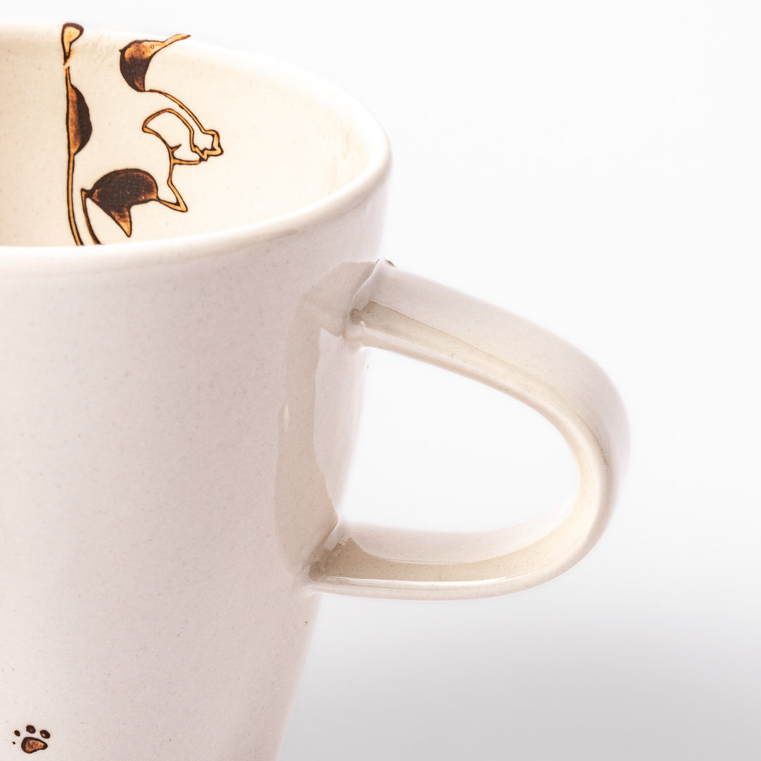 Cream-colored cup with a calico cat design reaching for a butterfly, decorated with dotted lines and paw prints.