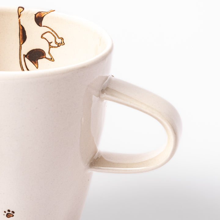 Cream-colored cup with a calico cat design reaching for a butterfly, decorated with dotted lines and paw prints.