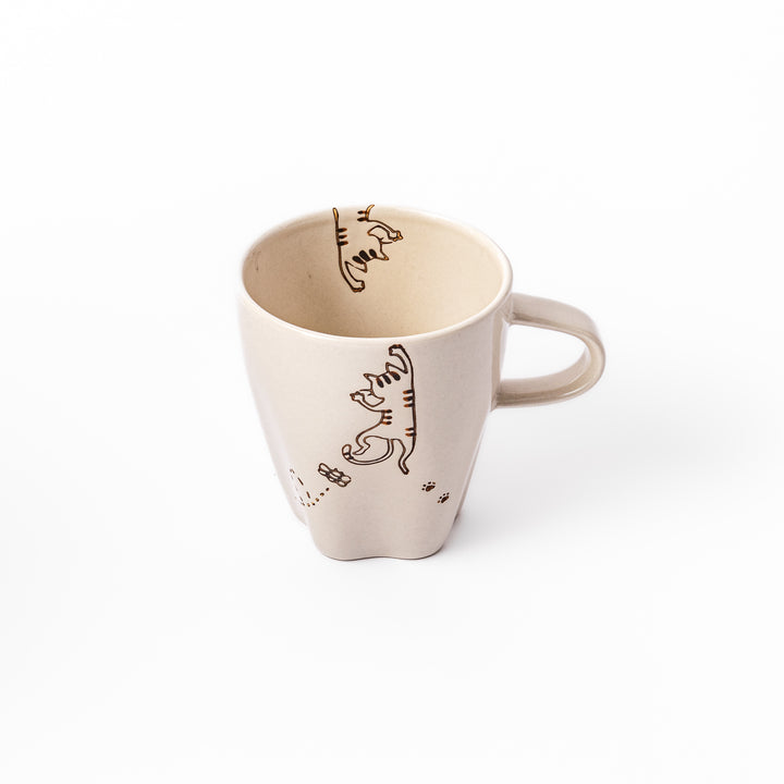 Cream-colored cup with a striped cat design reaching toward a butterfly, with dotted lines and paw prints.