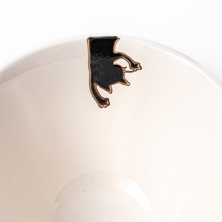 Cream-colored rice bowl with a black hanging cat, butterfly, and playful paw prints on the outside and inner rim.