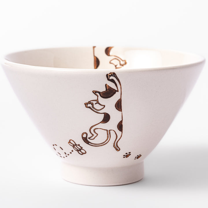 Cream-colored rice bowl with a calico hanging cat, butterfly, and playful paw prints on the outside and inner rim.