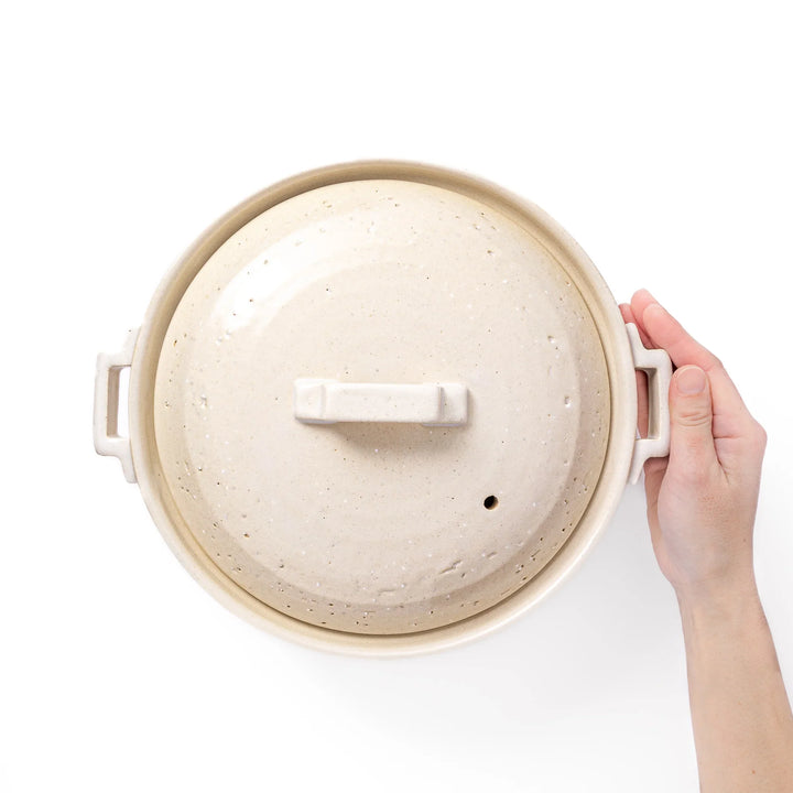 White Japanese donabe with a vented lid and side handles made of rustic handcrafted ceramic