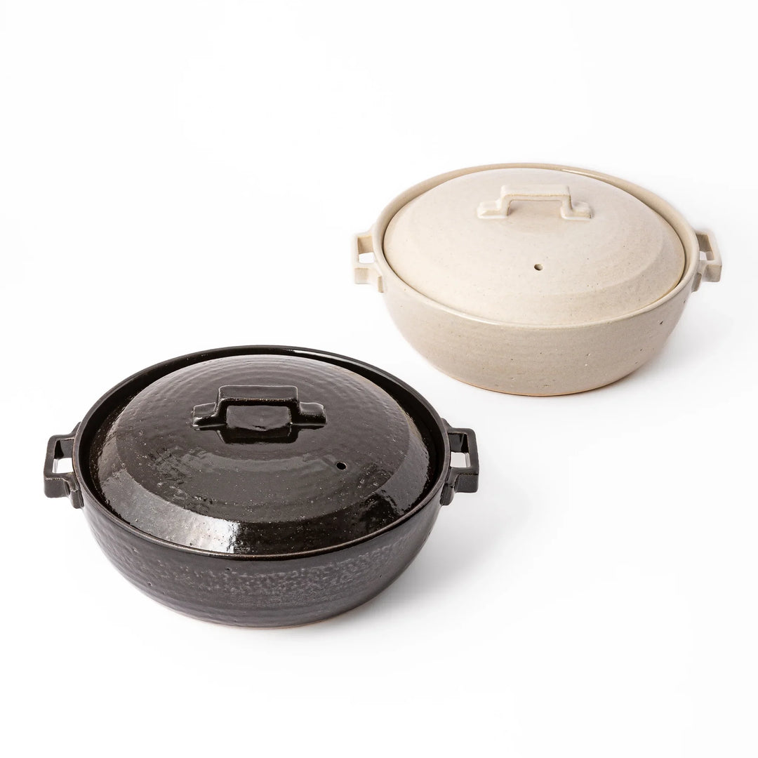 Black and beige Japanese ceramic donabe pots with fitted lids and side handles for stovetop cooking and family meals