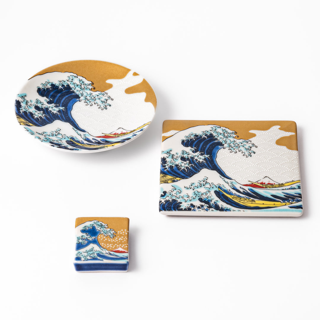 Japanese ceramic tableware set featuring Hokusai’s Great Wave design with vivid blue waves, golden sky, and Mt. Fuji, including sauce dish, coaster, and chopstick rest.