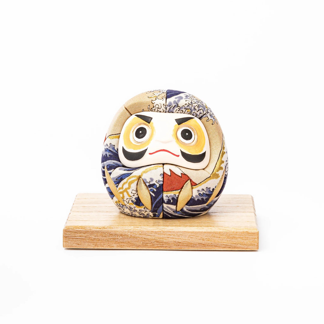 Fabric daruma ornament with bold Kabuki style face and wave pattern set on a small wooden display stand