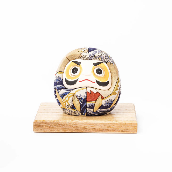 Fabric daruma ornament with bold Kabuki style face and wave pattern set on a small wooden display stand