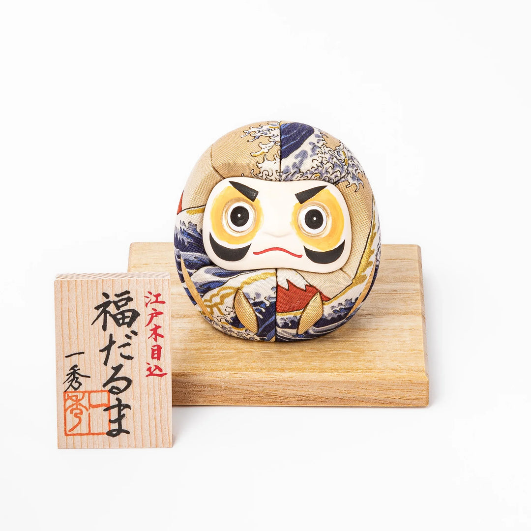 Fabric daruma ornament with bold Kabuki style face and wave pattern set on a small wooden display stand