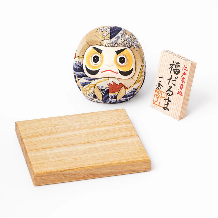 Fabric daruma ornament with bold Kabuki style face and wave pattern set on a small wooden display stand