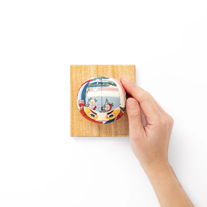 Fabric daruma ornament with bright multicolor kimono pattern and bold painted face displayed on a wooden stand