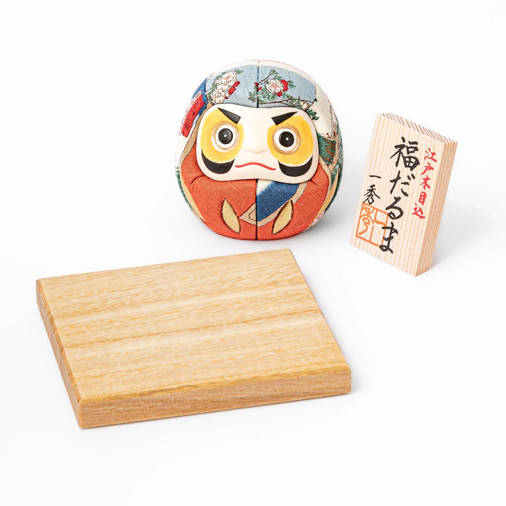 Fabric daruma ornament with bright multicolor kimono pattern and bold painted face displayed on a wooden stand