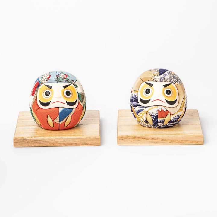 Two fabric daruma ornaments with multicolor kimono patterns displayed on wooden stands side by side
