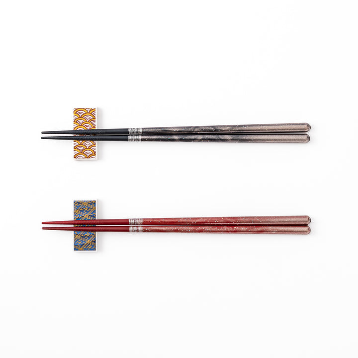 A pair of black and red lacquer Japanese chopsticks with two rectangular ceramic chopstick rests featuring traditional patterns