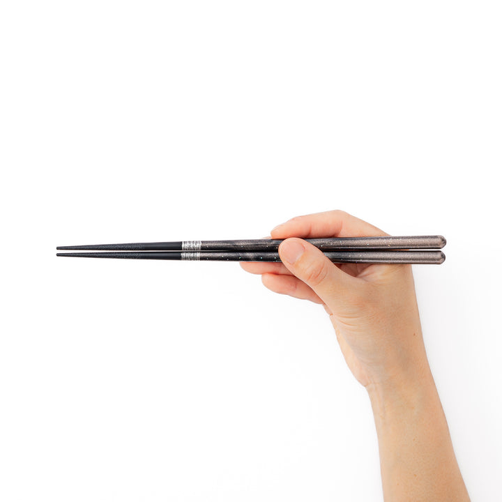 A hand holding a pair of black sparkling Japanese lacquer chopsticks to demonstrate a comfortable grip and standard length