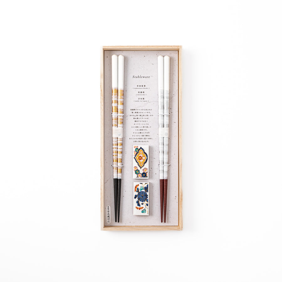 A pair of gold and silver textured Japanese chopsticks with two rectangular ceramic chopstick rests featuring floral patterns
