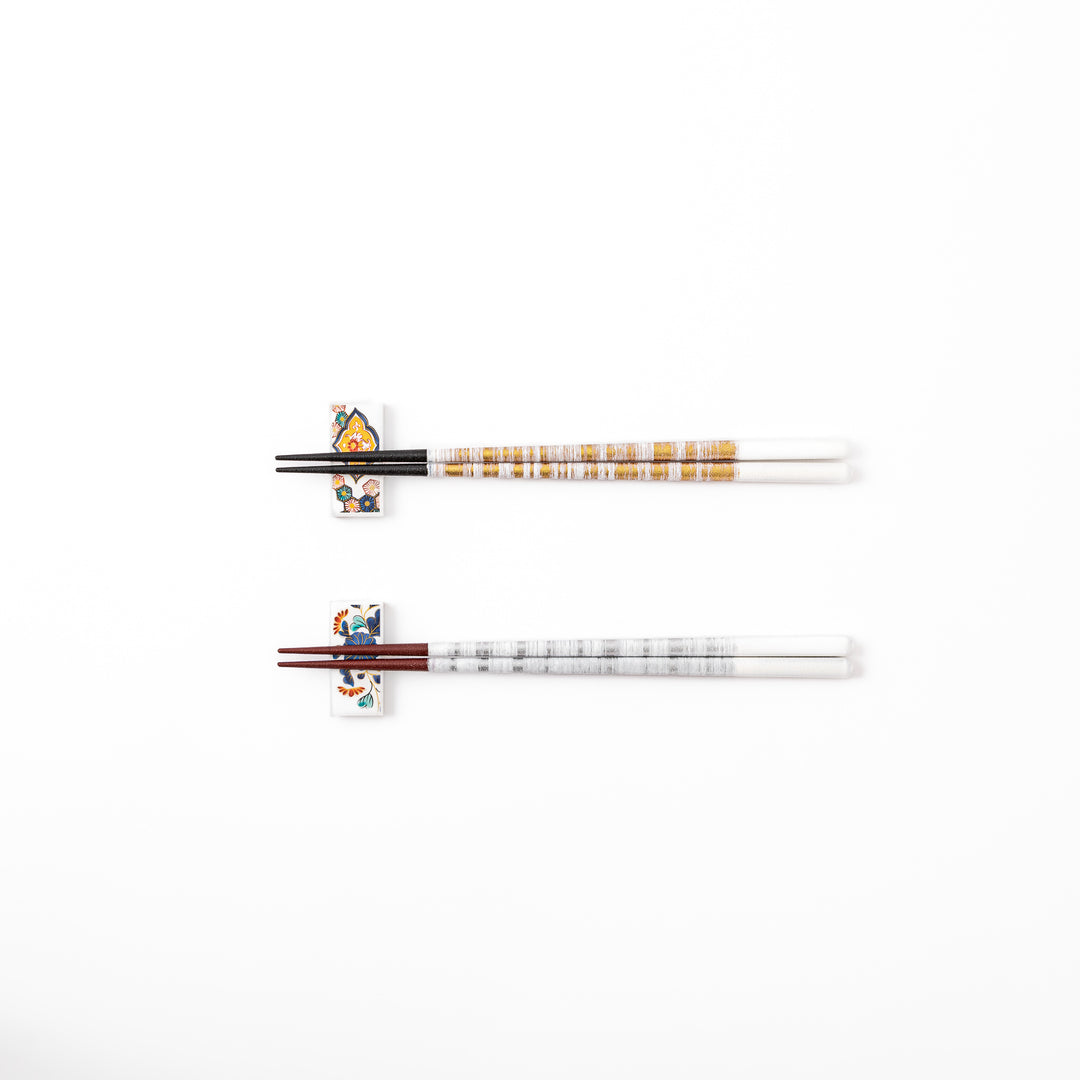 A pair of gold and silver textured Japanese chopsticks with two rectangular ceramic chopstick rests featuring floral patterns