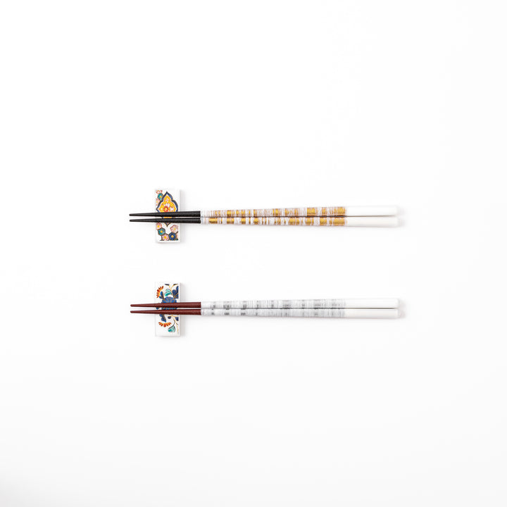 A pair of gold and silver textured Japanese chopsticks with two rectangular ceramic chopstick rests featuring floral patterns