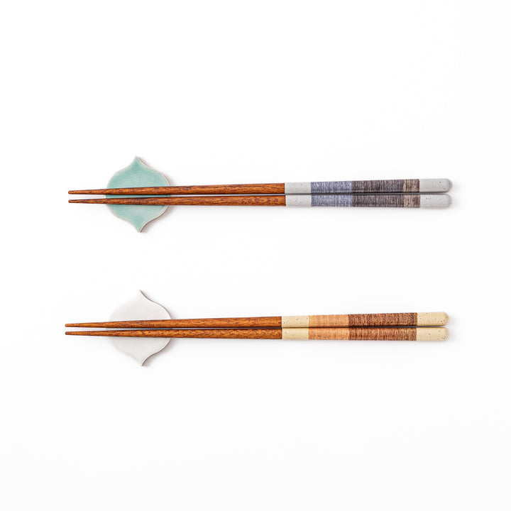 Two pairs of natural wood Japanese chopsticks resting on blue and white curved tile style ceramic chopstick rests