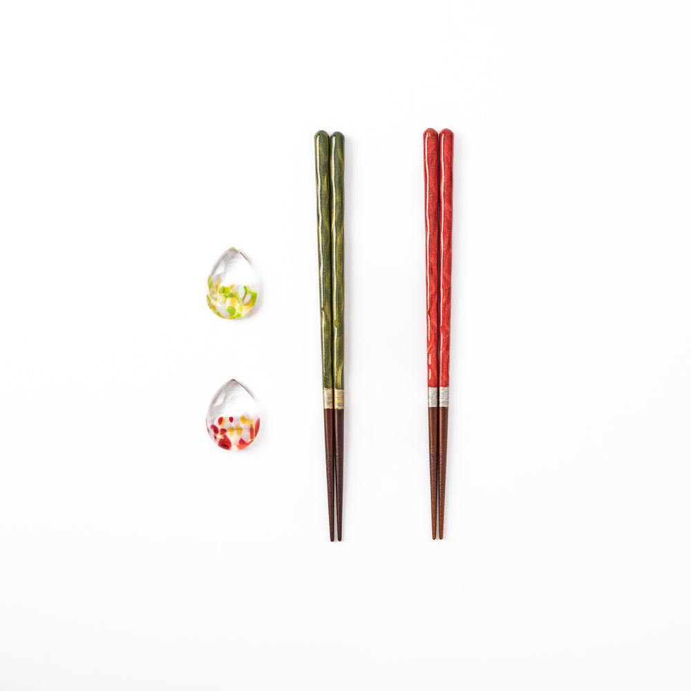 A pair of green and red Japanese lacquer chopsticks next to two teardrop shaped colorful translucent glass chopstick rests