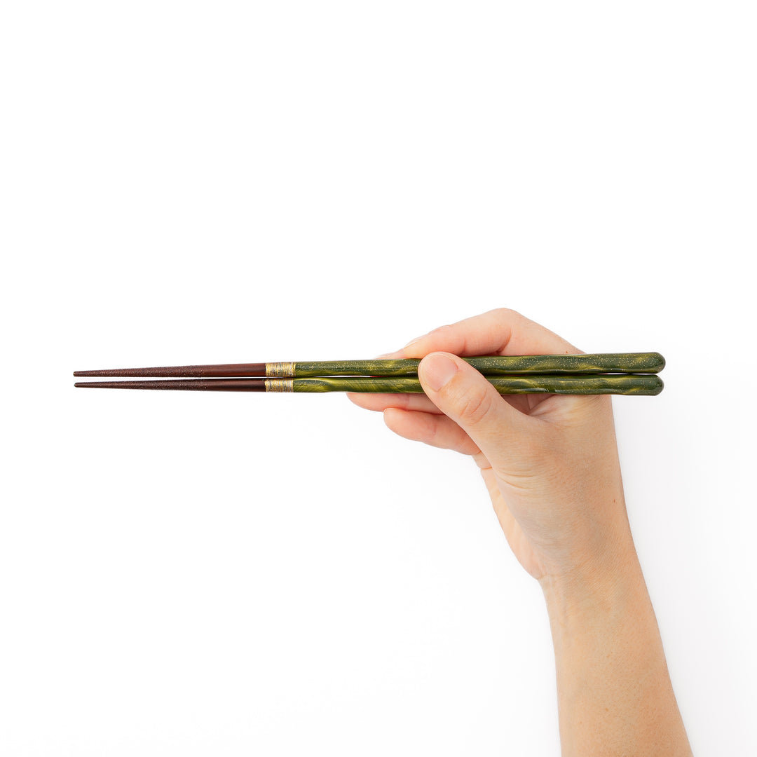 A hand holding a pair of glossy green Japanese lacquer chopsticks to demonstrate a comfortable natural grip and standard length