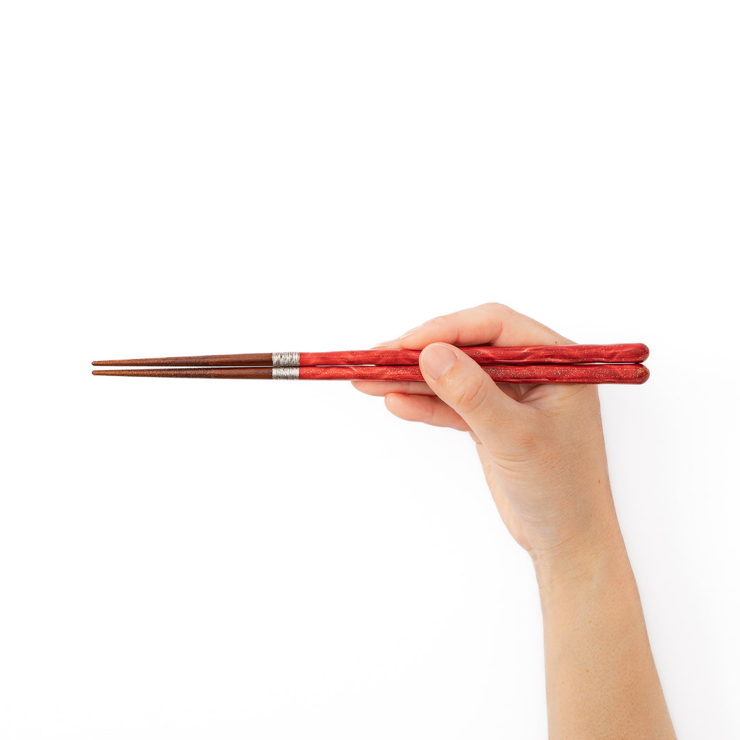 A hand holding a pair of glossy red Japanese lacquer chopsticks showcasing the vibrant festive color and elegant gold speckles