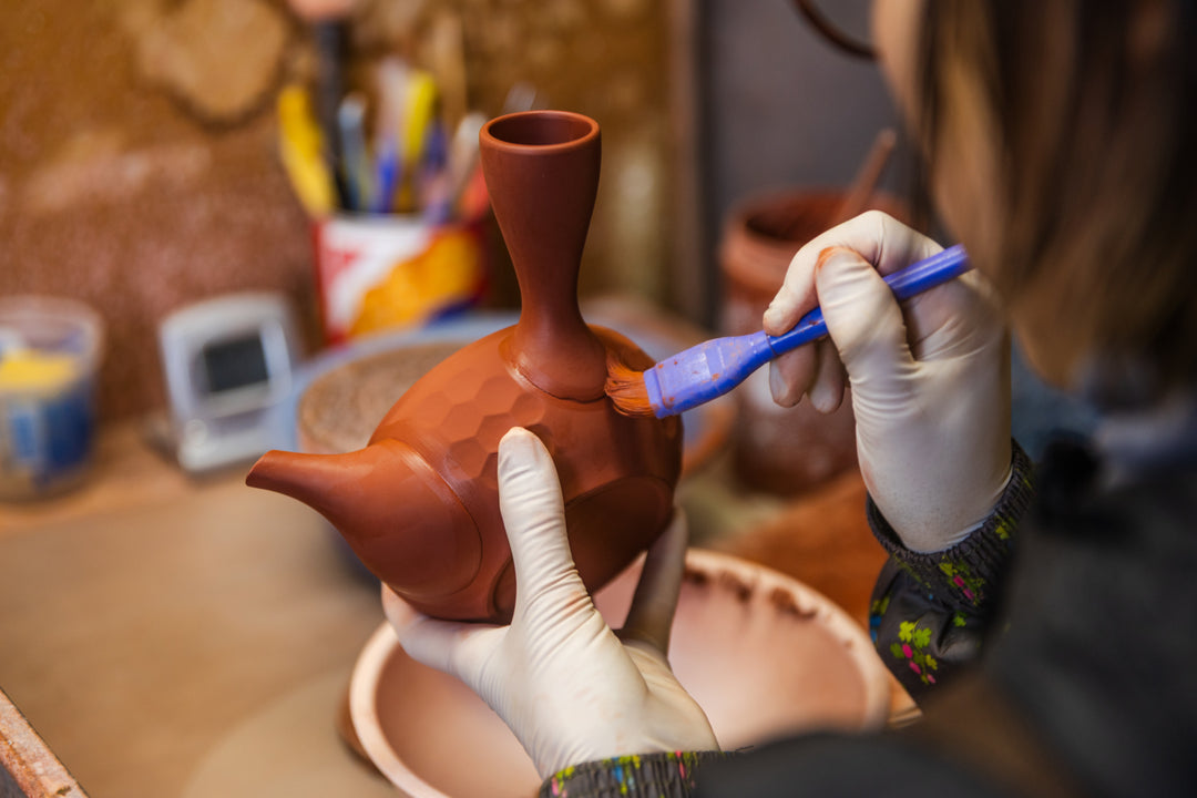 Handcrafting a Tokoname teapot as an artisan paints red clay with a brush, highlighting traditional Japanese pottery work.