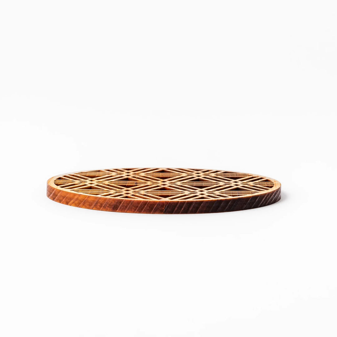 Round hinoki wood coaster with a sesame lattice cutout pattern, showcasing intricate geometric Japanese design.