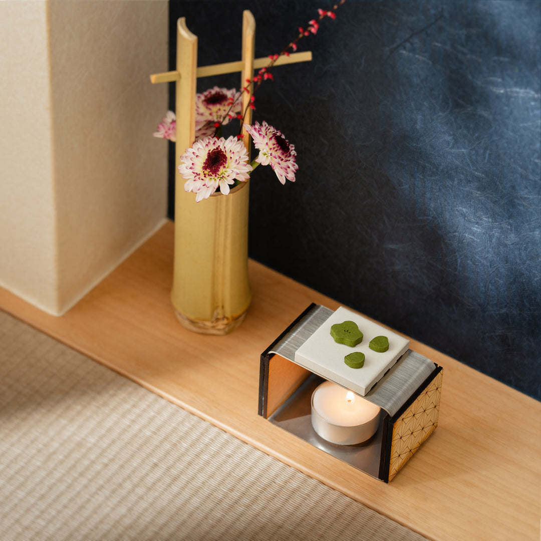 Green Japanese matcha pressed incense warming on a ceramic burner with a candle in a traditional tatami room setup