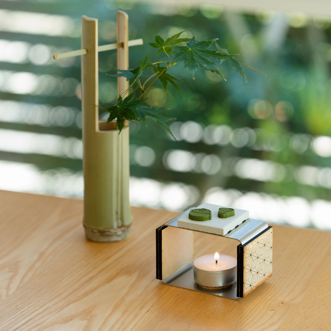 Teapot shaped green matcha pressed incense placed on a modern ceramic candle warmer with a bamboo vase background