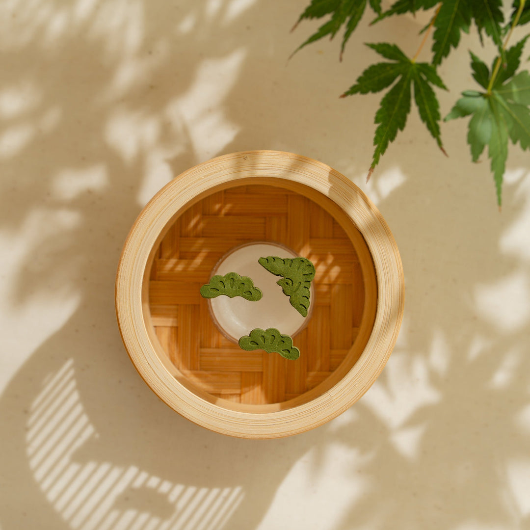 Green Japanese matcha pressed incense shaped like pine trees placed inside a round bamboo incense warmer