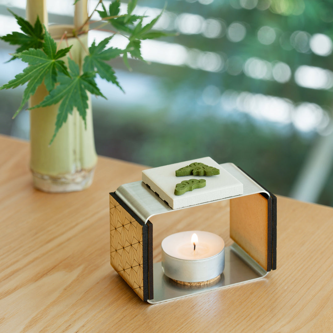 Pine shaped green matcha pressed incense placed on a modern ceramic burner with a lit candle on a wooden table