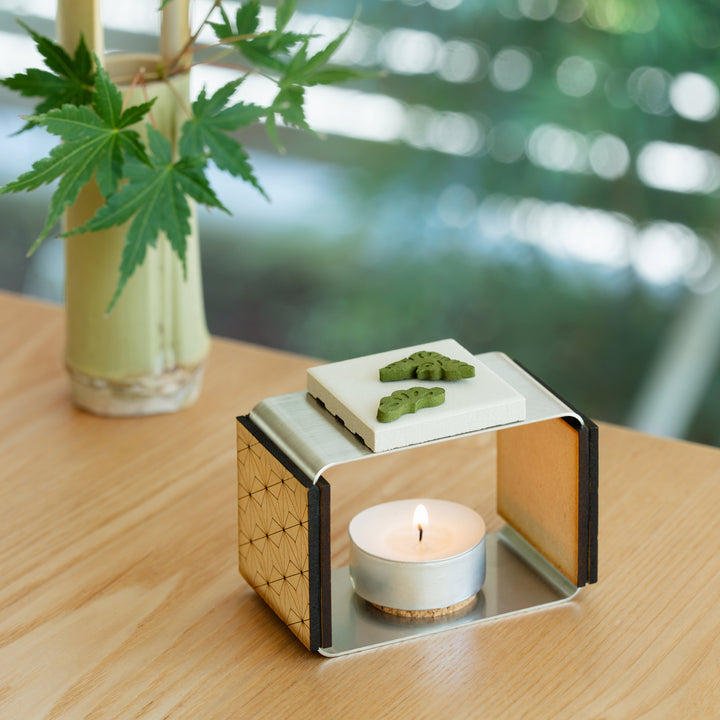 Pine shaped green matcha pressed incense placed on a modern ceramic burner with a lit candle on a wooden table