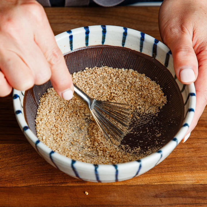 Nami from JOC using a Japanese stainless steel brush to gather ground sesame seeds inside a traditional Suribachi mortar
