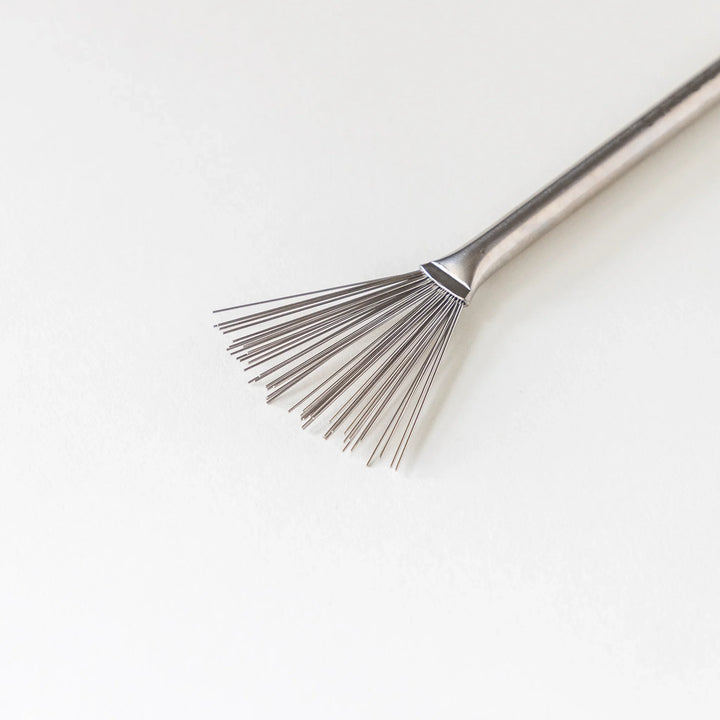 Close up view of fine wire bristles on a Japanese stainless steel grater brush on white background