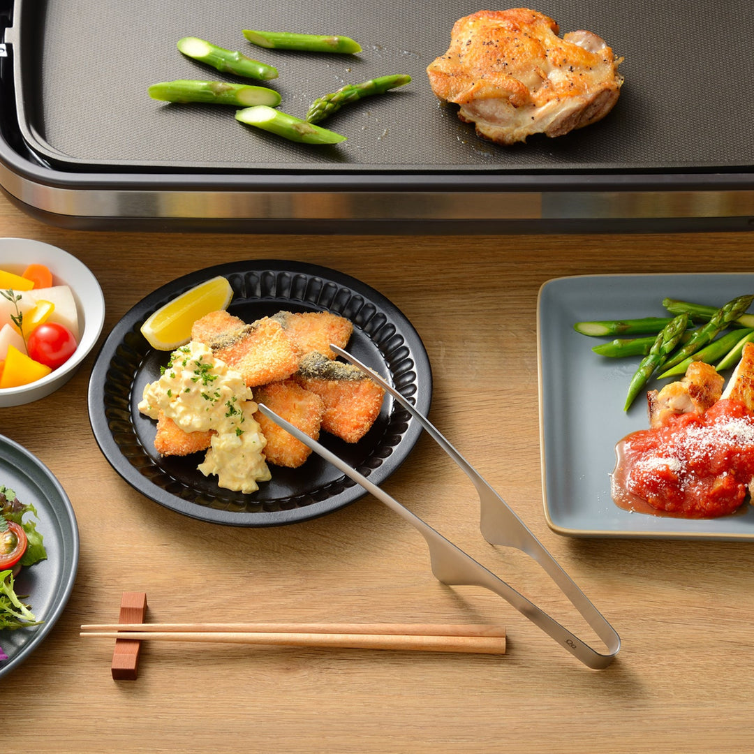 Hygienic stainless steel cooking tongs on a kitchen counter with elevated tips next to a stir fry pan and ingredients