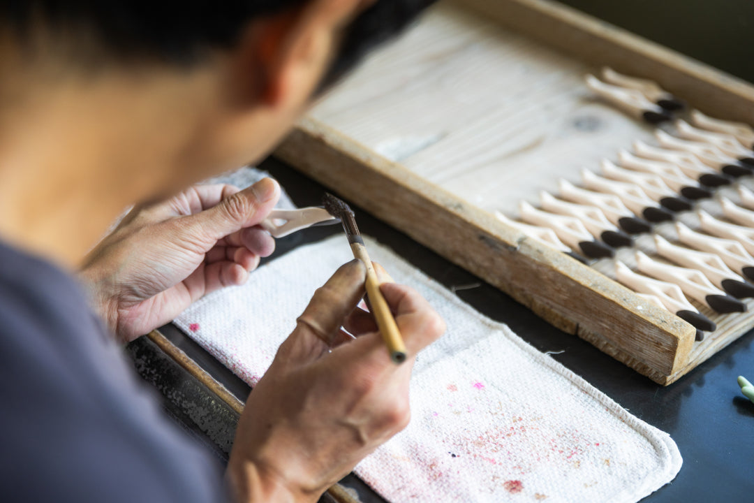 Artisan painting small ceramic chopstick rests in a workshop, adding hand-painted details with a fine brush.