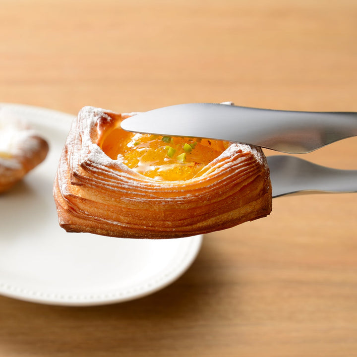 Japanese bread tongs gently picking up a delicate fruit danish pastry without damaging the flaky layers or toppings