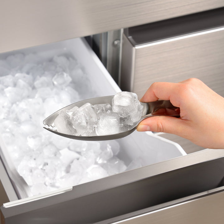 Japanese stainless steel ice scoop tongs scooping multiple ice cubes from a freezer drawer for efficient serving