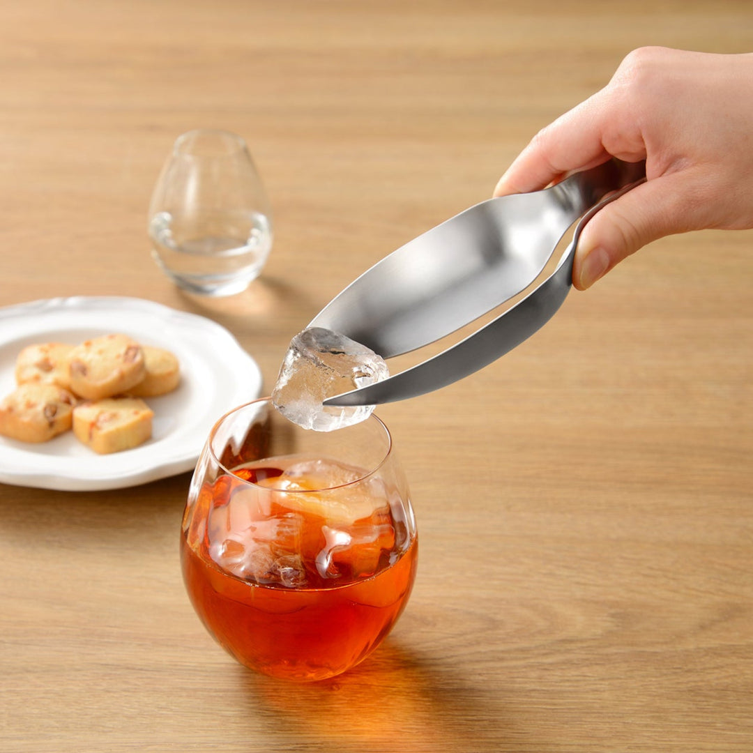 Japanese stainless steel tongs placing a single ice cube into a glass of iced tea to demonstrate precision control