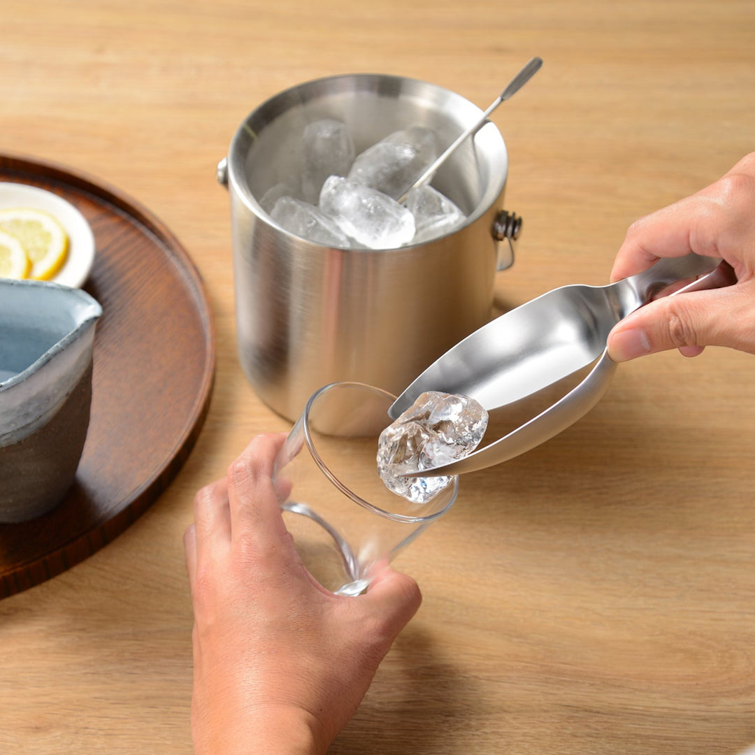 Serving ice from a stainless steel bucket with scoop tongs into a glass for a relaxing home bar experience