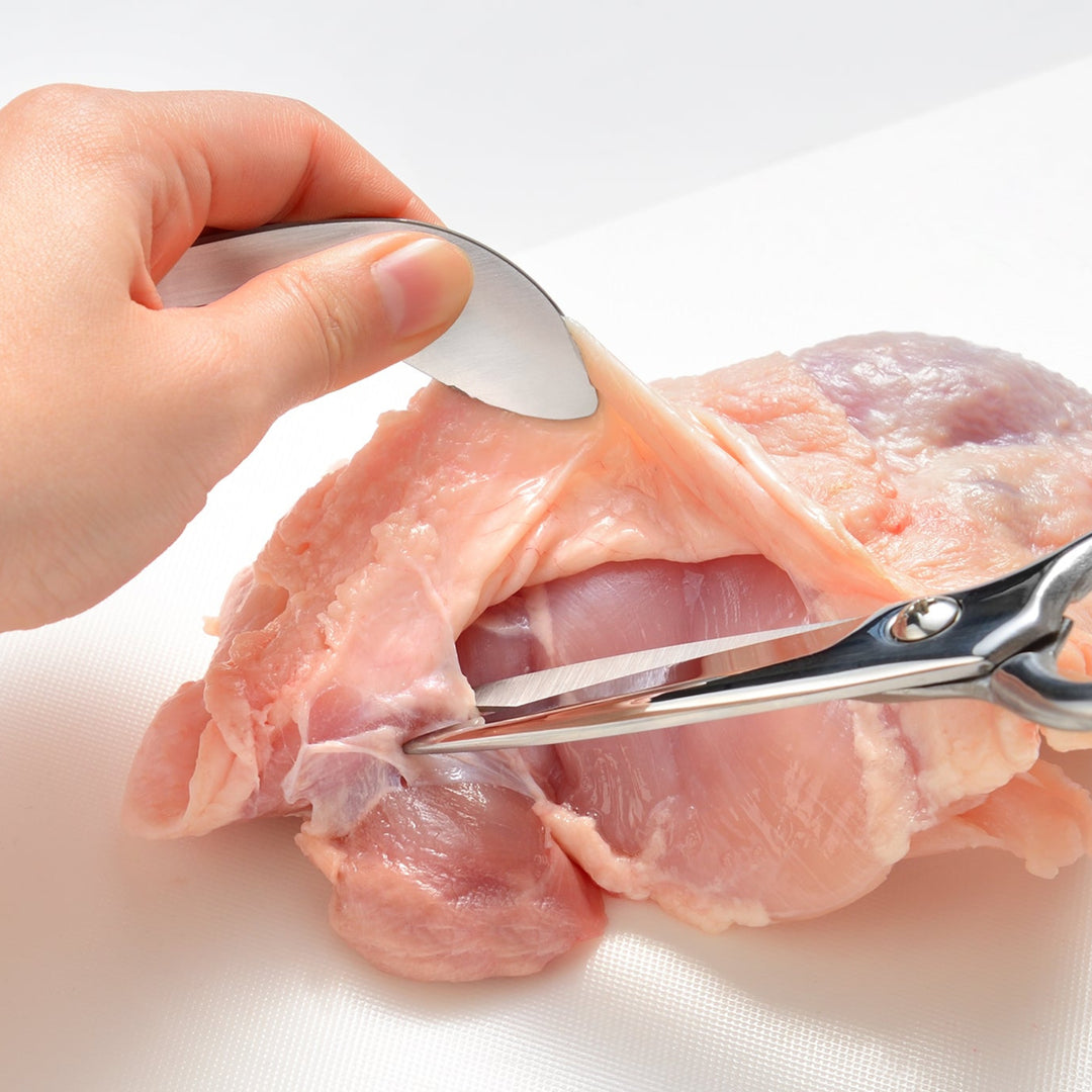 Using Japanese fingertip tongs to hold raw chicken while cutting with kitchen shears to keep hands clean and hygienic