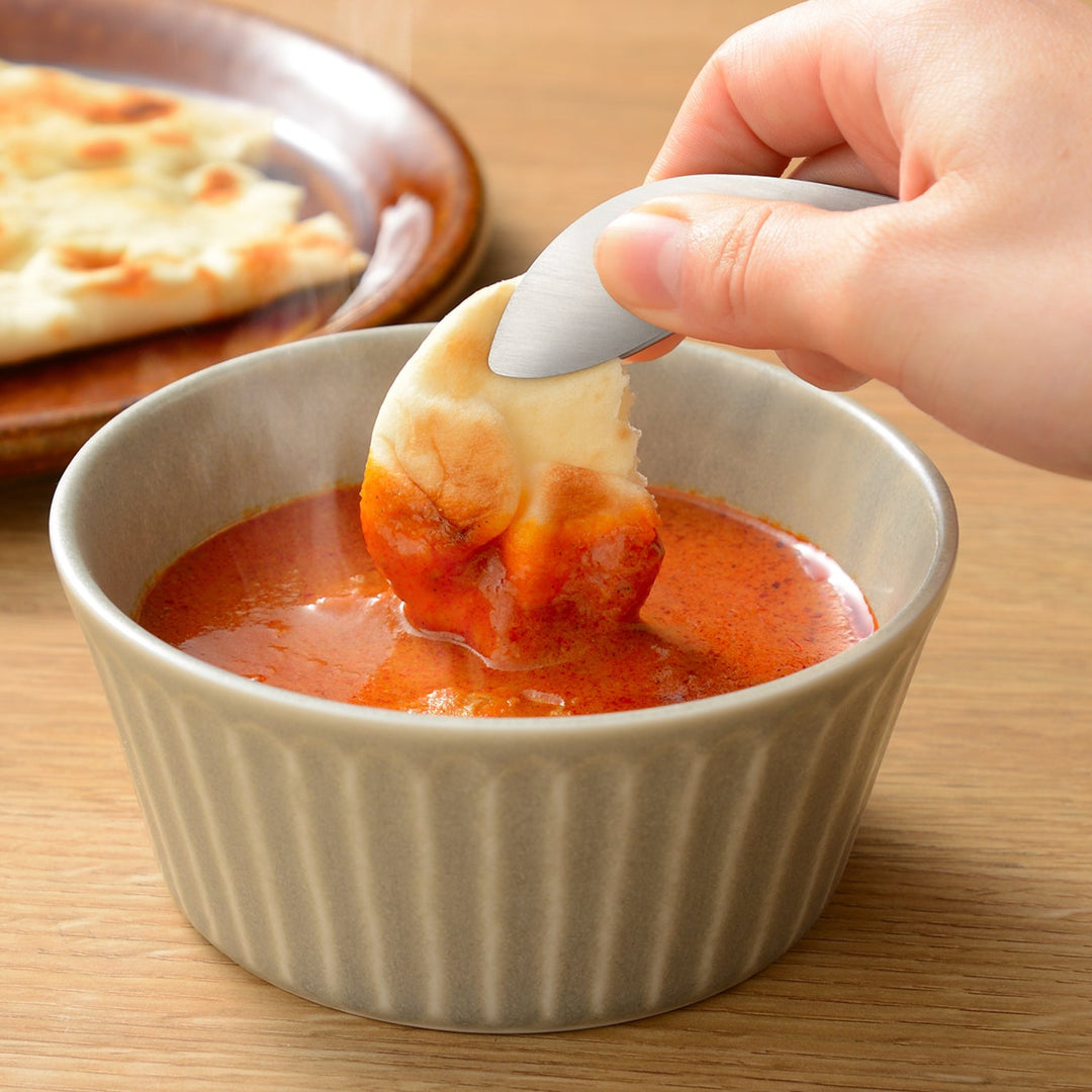 Small stainless steel fingertip tongs dipping a piece of naan bread into curry to avoid messy fingers while eating