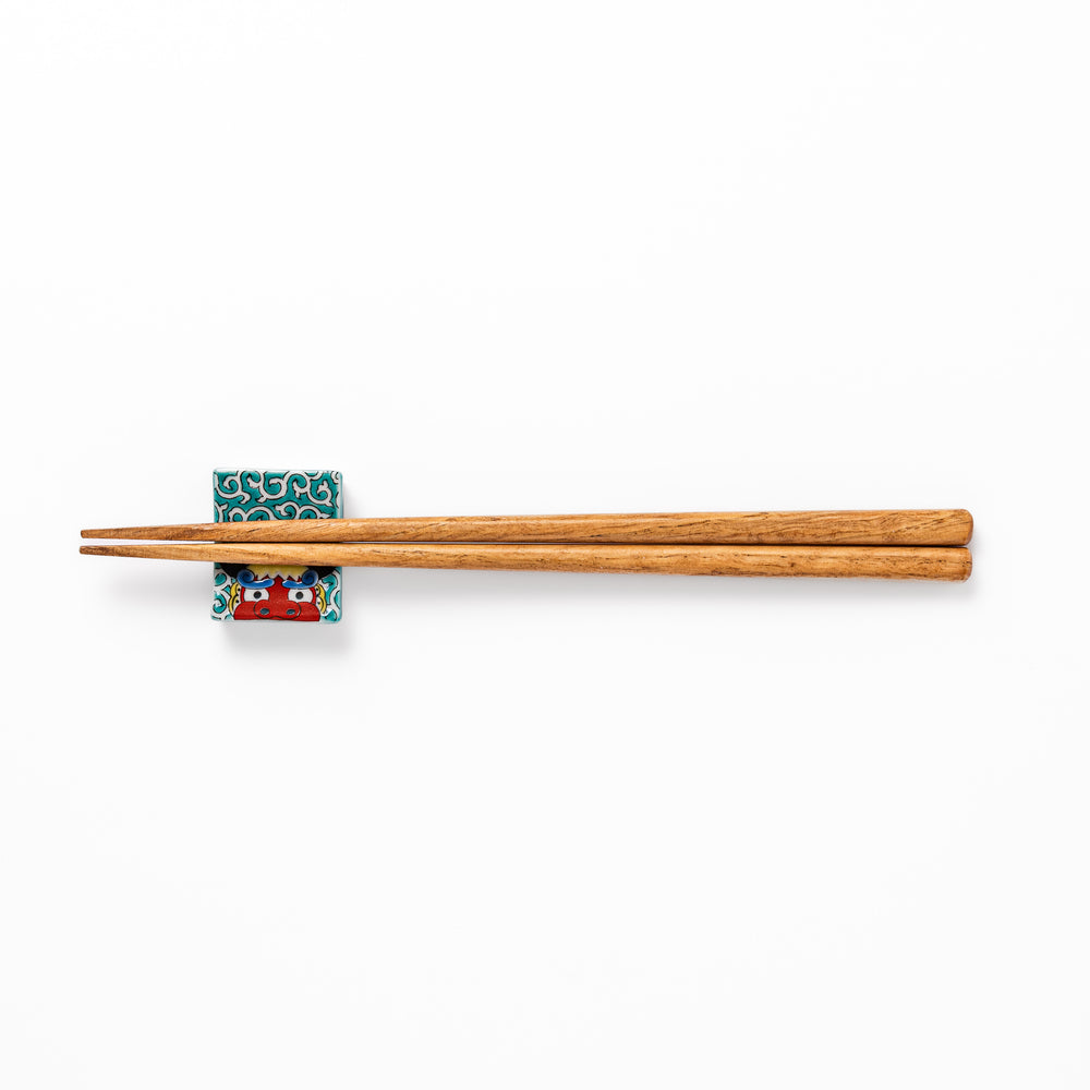 Rectangular Japanese ceramic chopstick rest featuring a bold red lion dance motif with green swirl background, adding festive tradition to dining tables.