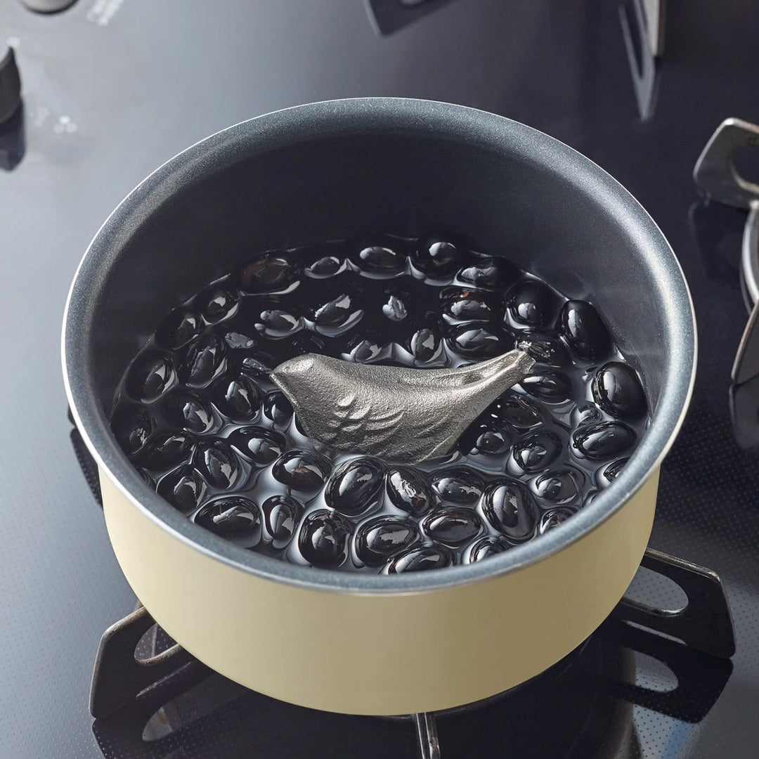 Bird shaped cast iron supplement submerged in a pot of simmering black soybeans on a gas stovetop