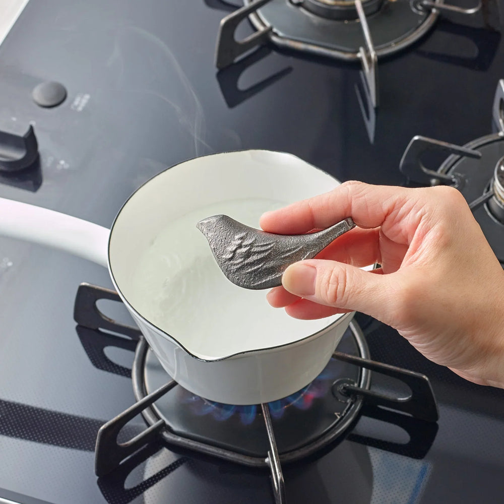 Person placing a bird shaped cast iron supplement into a pot of water heating on a gas stove burner