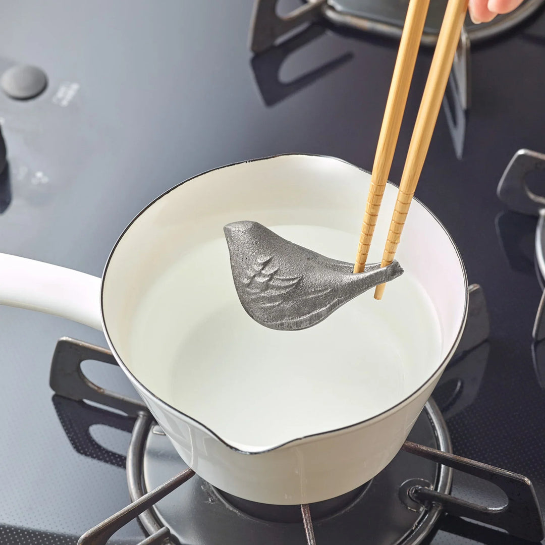 Person easily lifting a bird shaped cast iron supplement out of a pot using wooden chopsticks